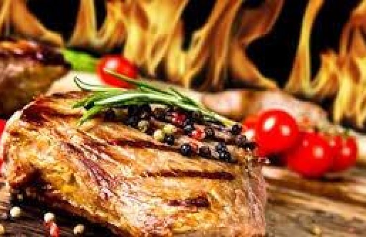 Grilled steak with herbs and peppercorns in front of open flames