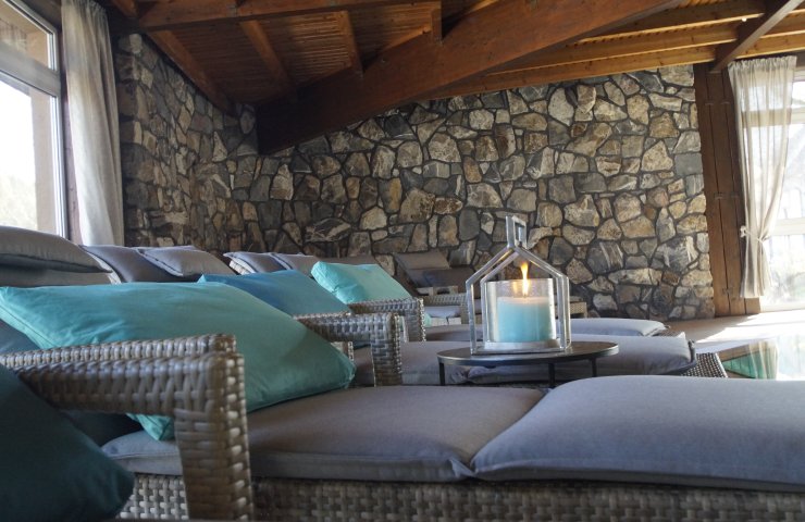 Relaxation area with loungers, turquoise cushions and a natural stone wall beneath a wooden ceiling