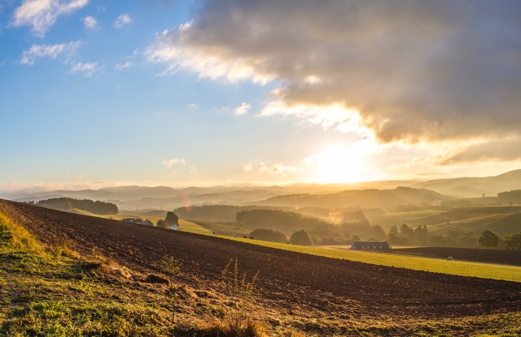 Wide view over fields and wooded hills in the Sauerland with the sun low in the sky