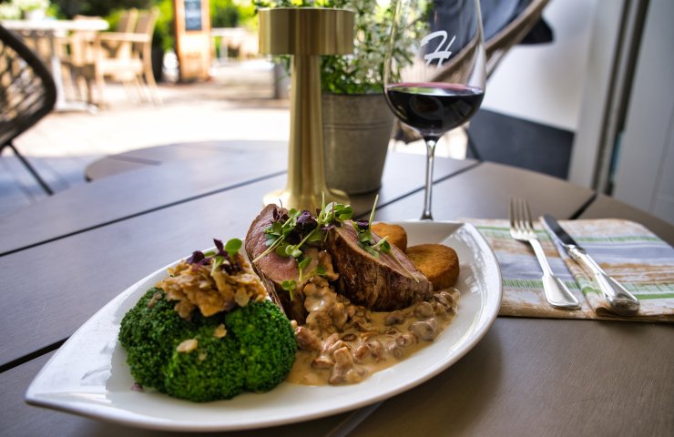 Pink-roasted meat with creamy chanterelle sauce, broccoli and potato rösti, with a glass of red wine on the terrace