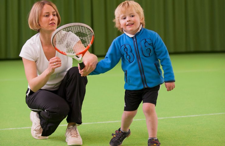 Tennis coach showing a small boy how to hold a racket in the indoor tennis hall