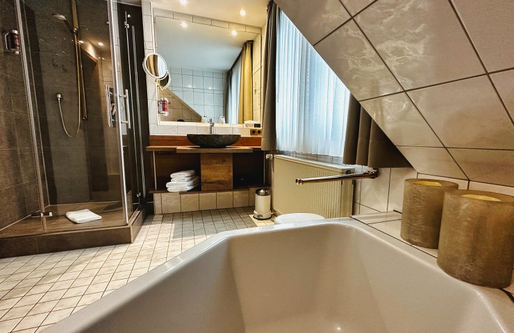 Bathroom with bath under the sloping roof, glass shower and stone basin on a wooden washstand
