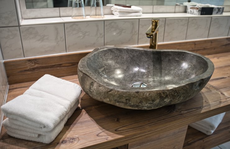 Natural stone basin with gold tap on a wooden washstand, with towels beside it