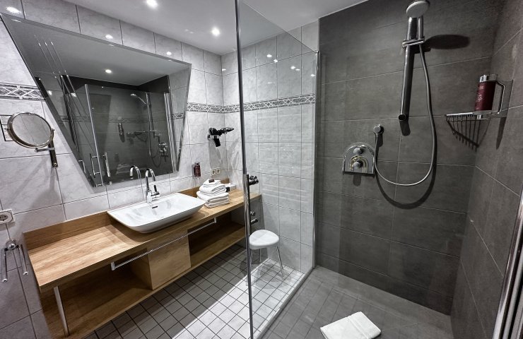 Bathroom with a large tiled glass shower, washbasin on a wooden vanity and a cosmetic mirror