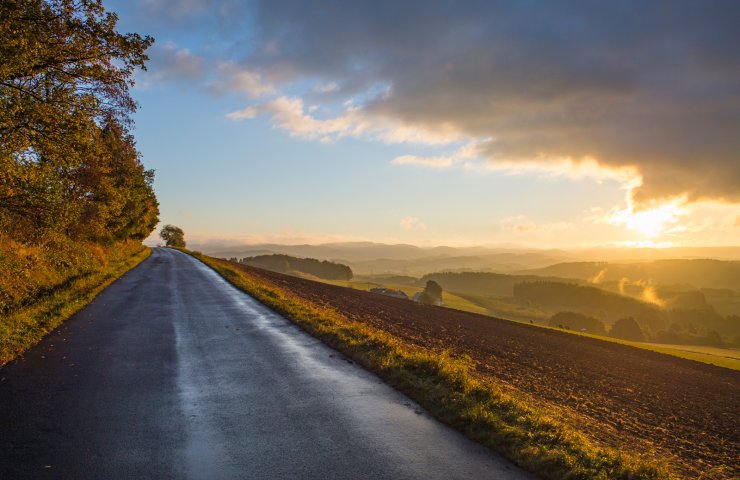 Narrow country road beside a field, looking out over the Sauerland hills in the evening light