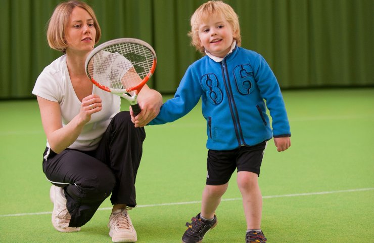 Tennis coach showing a small boy how to hold a racket in the indoor tennis hall