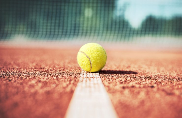 Tennis ball on the line of a clay court, with the net in the background