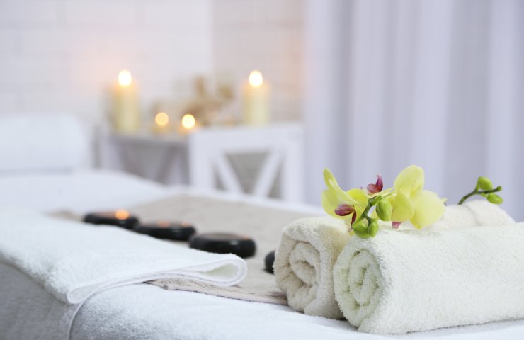 Massage table with rolled towels, an orchid, hot stones and candles in the background