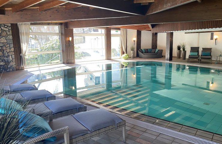 Indoor pool at Hotel Hennemann with a wooden ceiling, loungers by the pool and large windows
