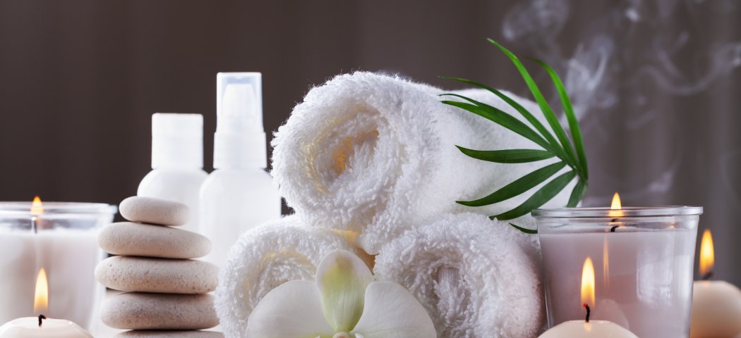 Spa still life with rolled towels, candles, massage stones and an orchid flower
